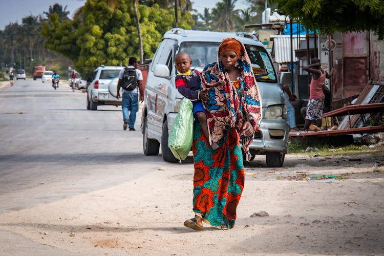 Photo Of A Woman Carrying Her Child While Walking