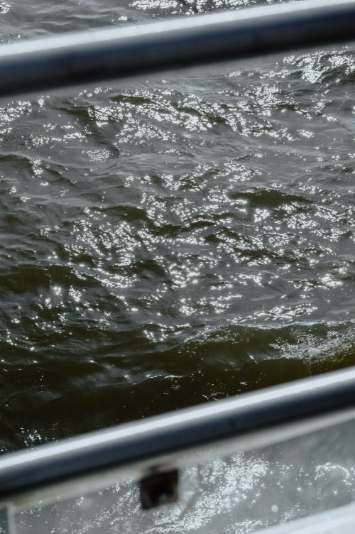 Free Shimmering sunlight on the water viewed through a boat rail, creating a serene seascape. Stock Photo