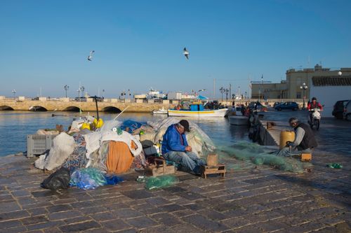 Free Local fishermen repairing nets at Gallipoli harbor, capturing traditional maritime life in Puglia, Italy. Stock Photo