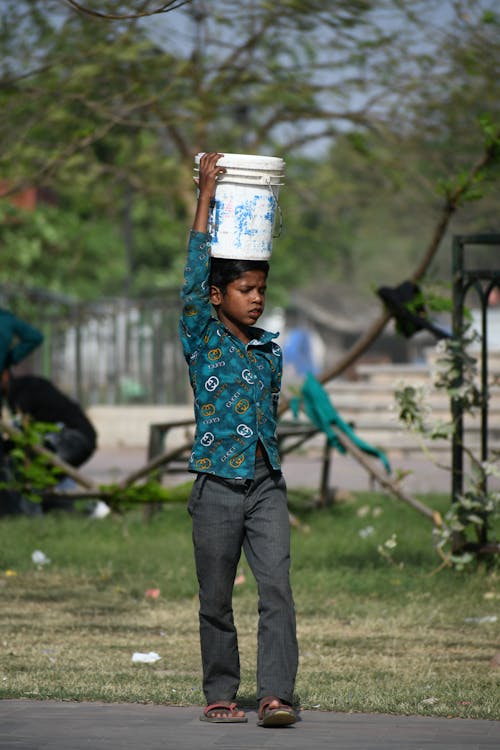 Photo of a Boy Carrying a Bucket on His Head
