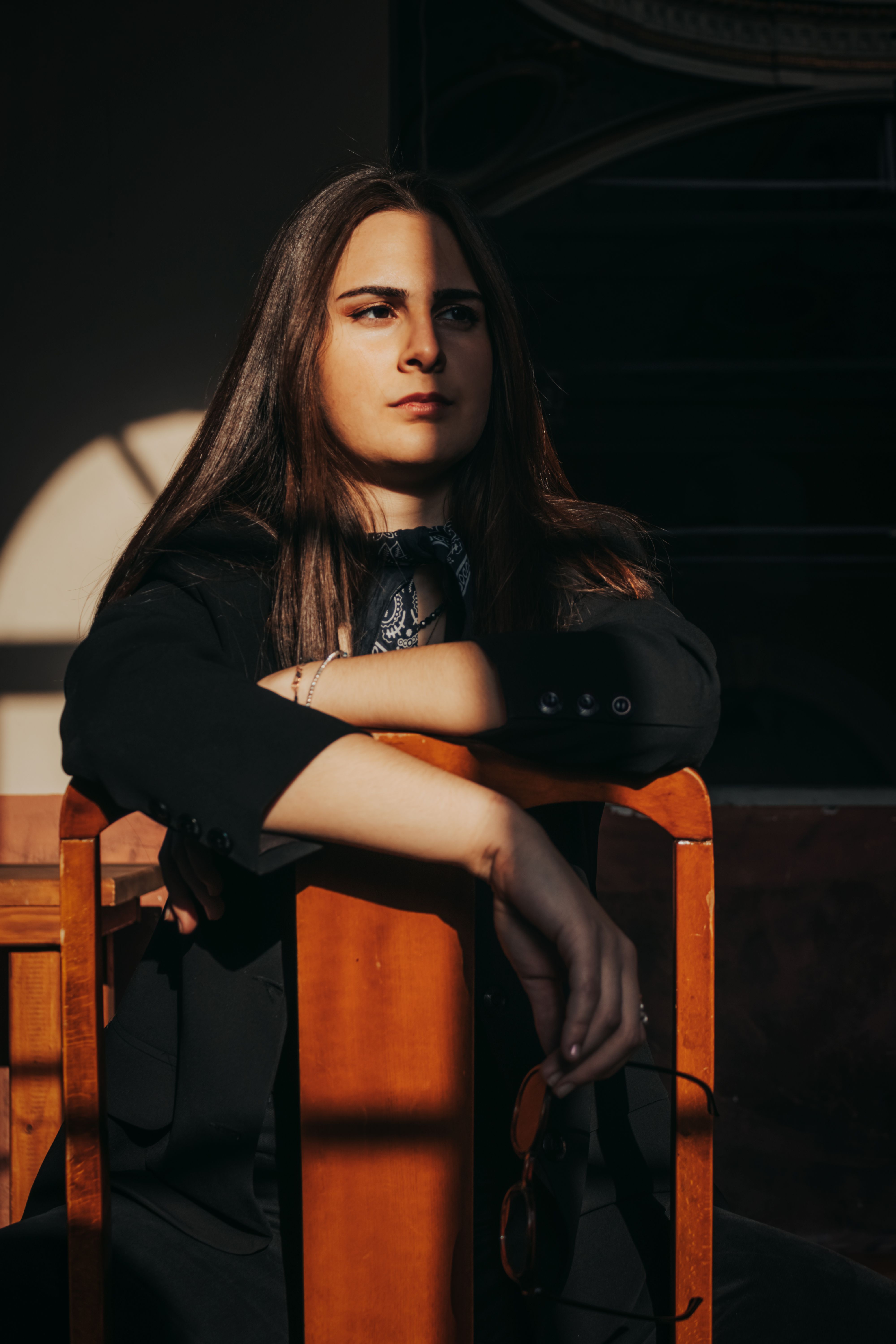Portrait of a young woman sitting indoors with natural light and shadows, creating a thoughtful atmo