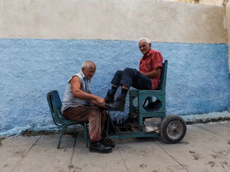 Street scene of a shoeshiner at work, polishing a customer's shoes outdoors.