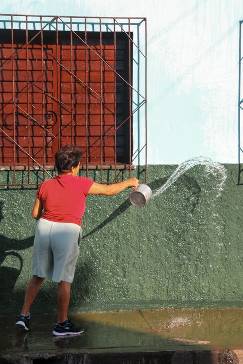 Free A woman in casual attire throwing water from a bucket against a wall outdoors in bright daylight. Stock Photo