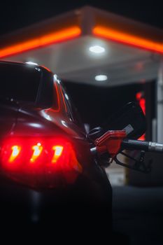 A close-up view of a car being refueled at a gas station at night with glowing tail lights.