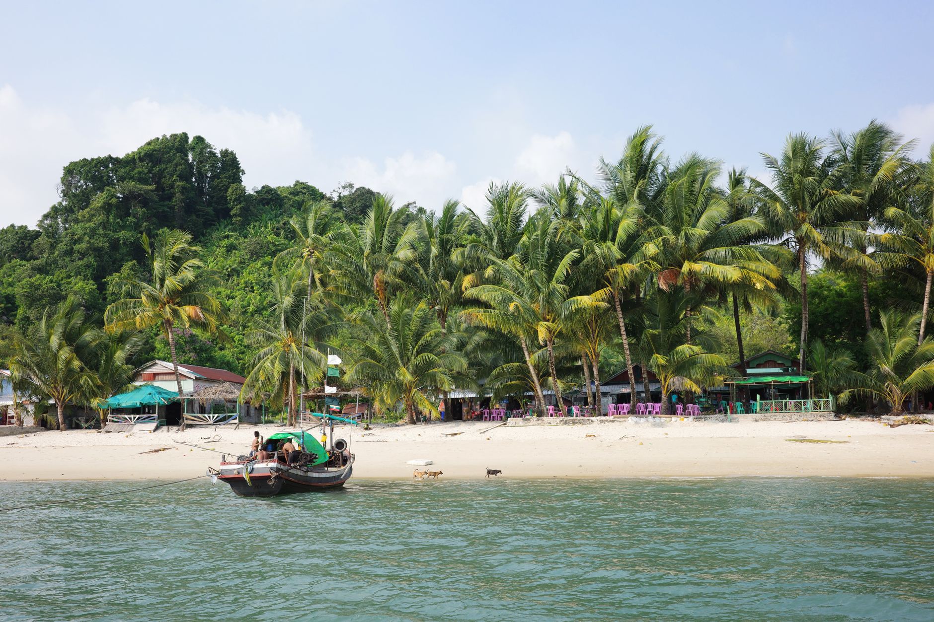 A serene beach with palm trees and traditional boat in Myeik, Myanmar.