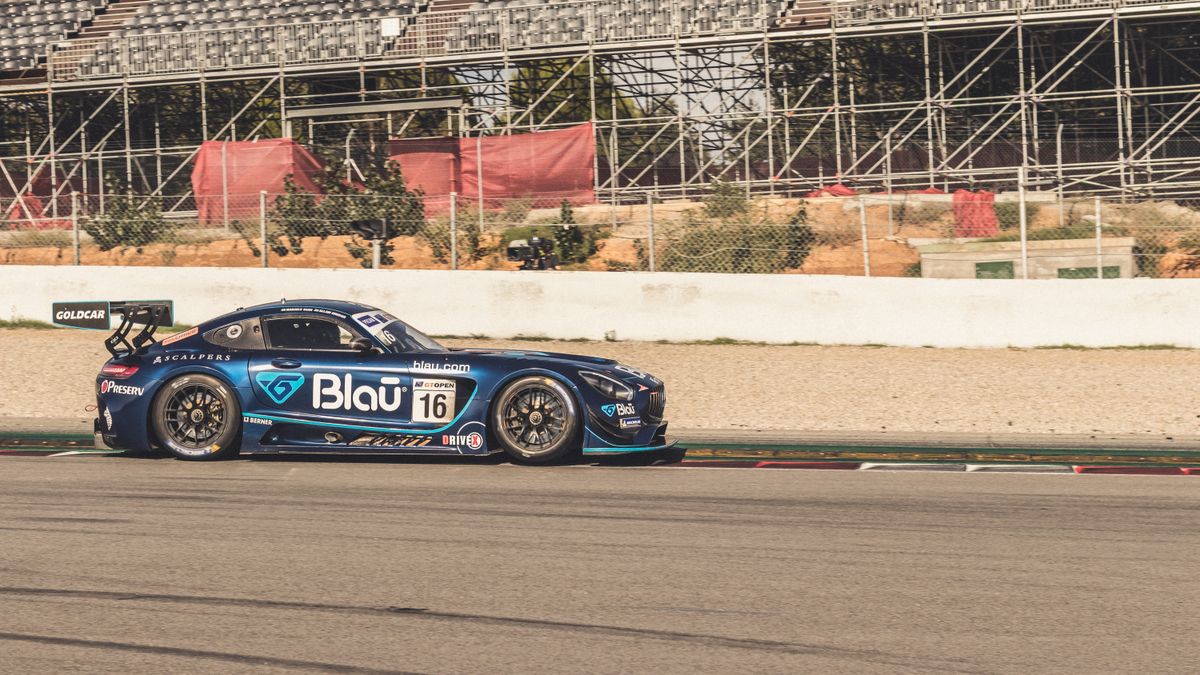 Blue racing car speeds on a track against a backdrop of empty stands.
