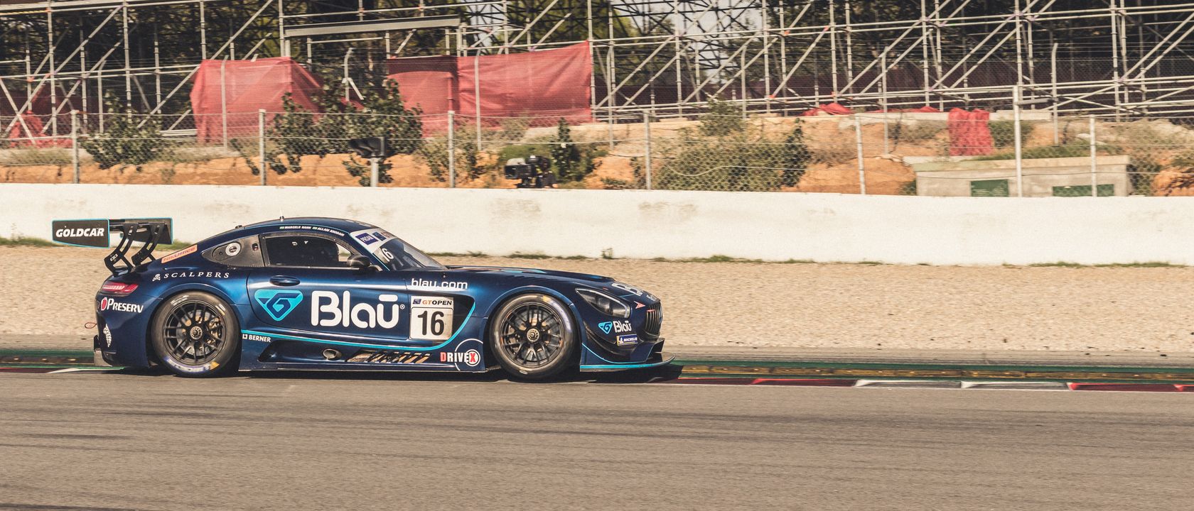 Blue racing car speeds on a track against a backdrop of empty stands.