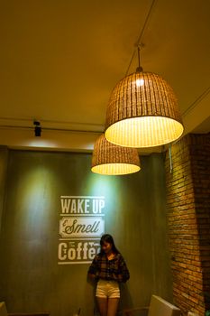 Warm coffee shop scene with woven lamps and a woman standing against decor wall.