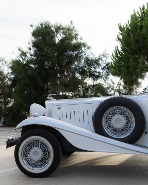 Free Elegant side view of a vintage white classic car parked outdoors among trees. Stock Photo