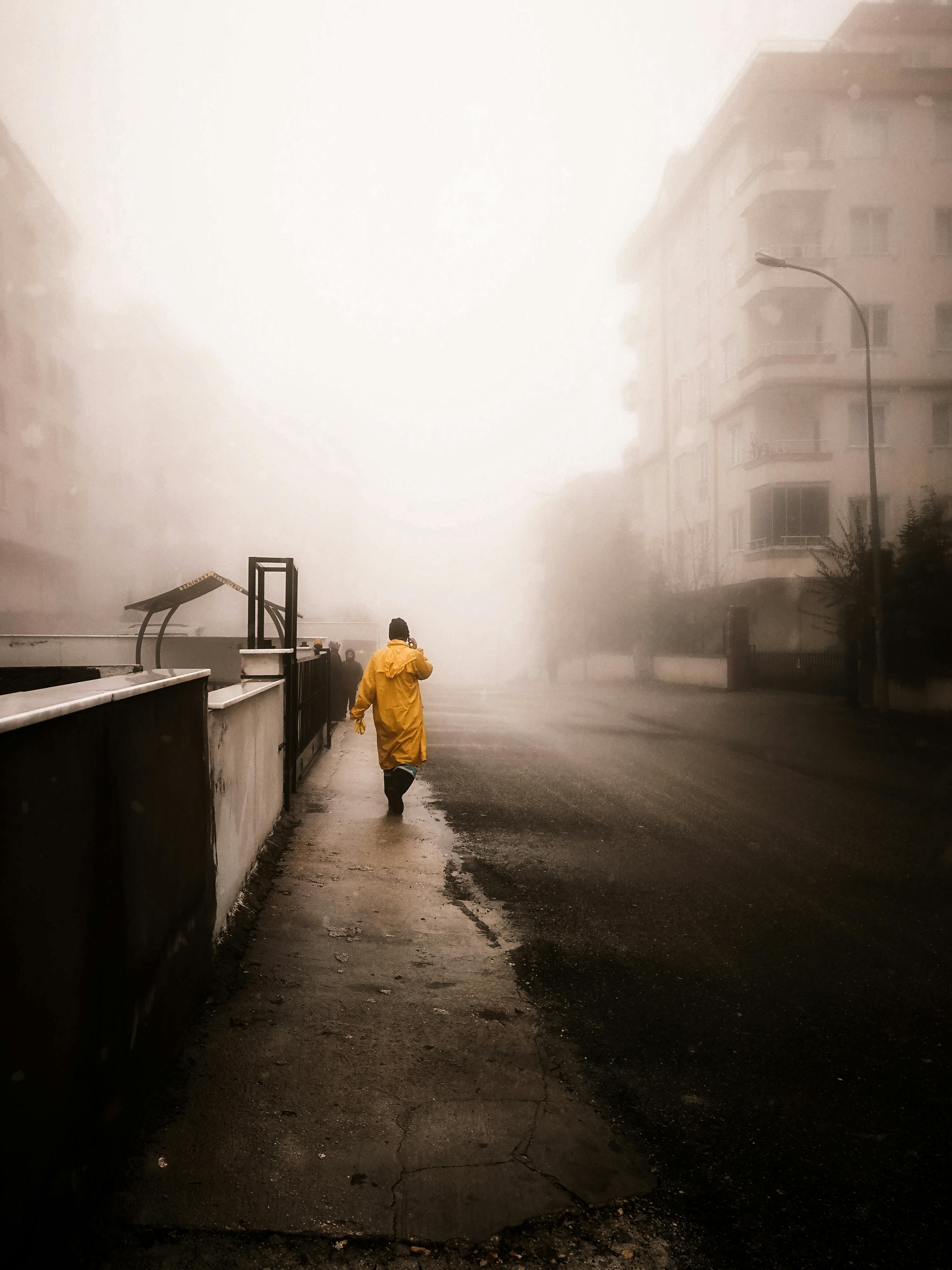 A solitary figure in a yellow raincoat walking on a foggy city street, creating a mysterious urban atmosphere.