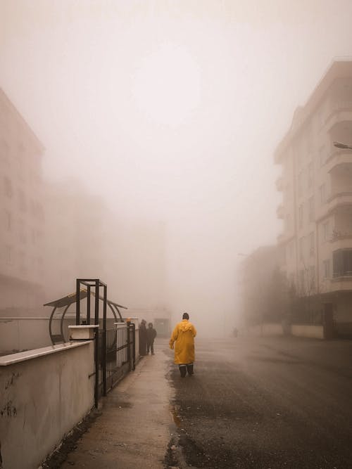 Free A Man in a Yellow Raincoat Walking in a Foggy Neighborhood Stock Photo