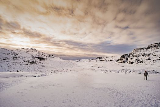 A lone adventurer walks on a vast snowy terrain in Iceland during winter at sunset.