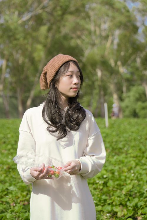 Free A young woman in a beanie holding strawberries outdoors on a sunny day. Stock Photo