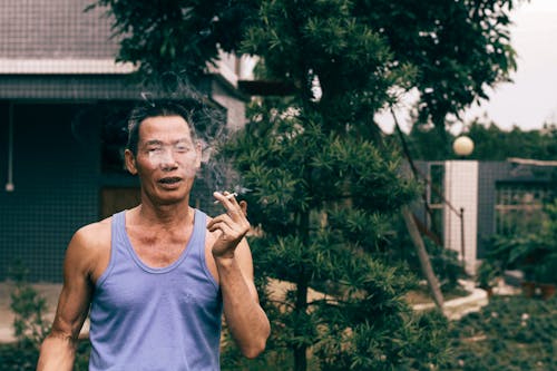 Man in Blue Tank Top Smoking Cigarette