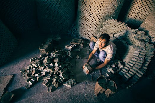 A man with short hair working and stacking bricks in a dimly lit warehouse.
