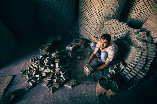 Free A man with short hair working and stacking bricks in a dimly lit warehouse. Stock Photo