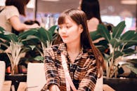 一位迷人的亚洲年轻女子坐在咖啡馆里，四周环绕着郁郁葱葱的绿植