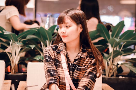 一位迷人的亚洲年轻女子坐在咖啡馆里，四周环绕着郁郁葱葱的绿植