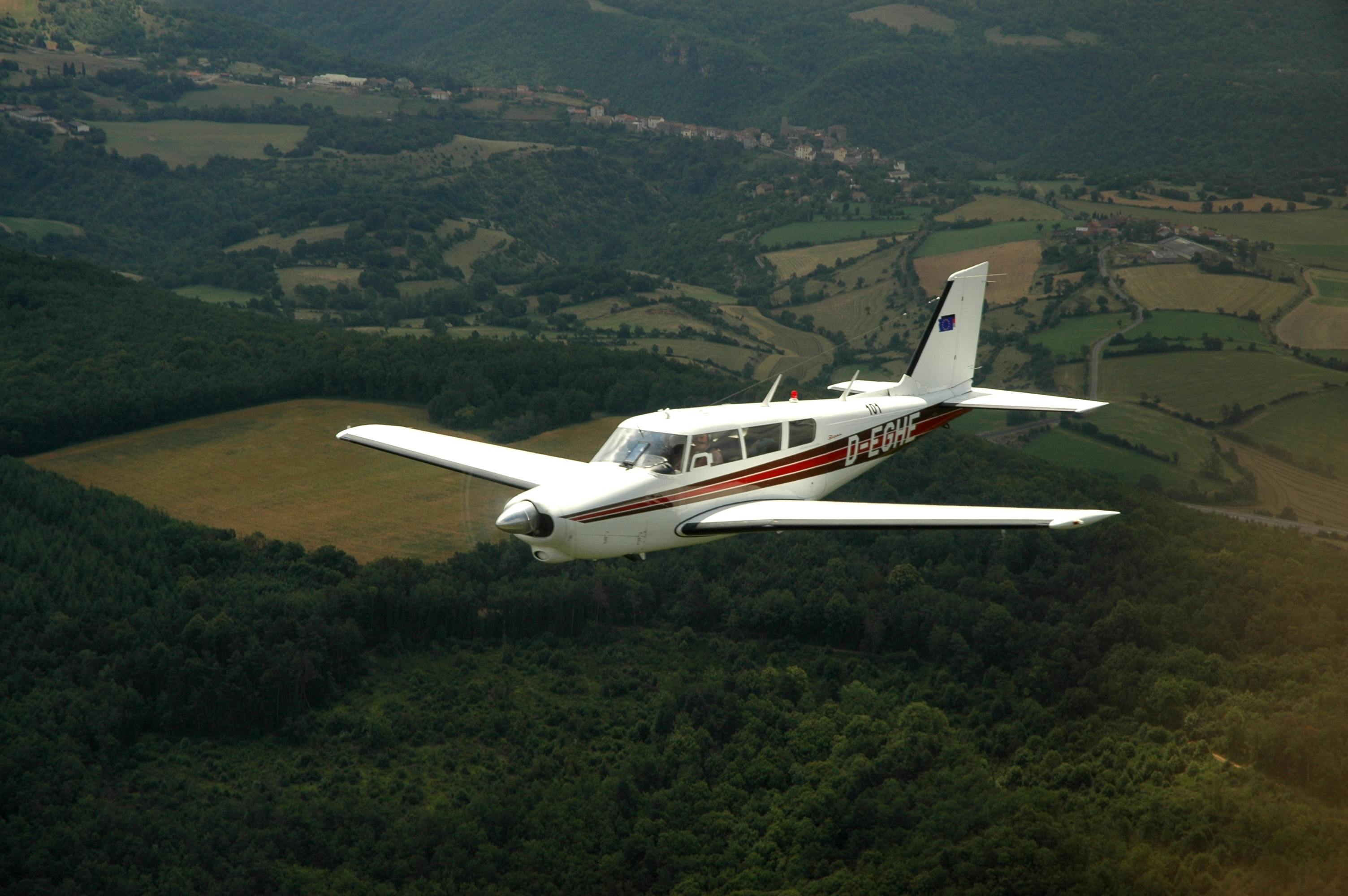 Free Small aircraft flying over lush green countryside, showcasing scenic aerial view. Stock Photo