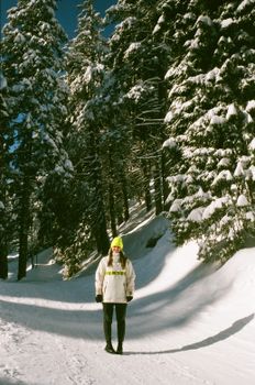 A woman in bright winter clothes stands amidst snow-covered trees in a serene forest.