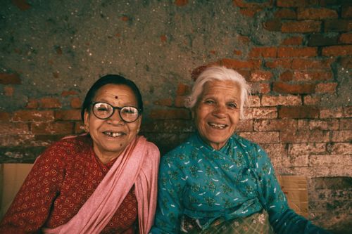 Free Capture of two elderly women sharing joyful smiles against a rustic brick wall. Stock Photo