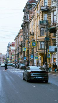 A black car drives down a city street lined with historic buildings, capturing urban life in a busy setting.