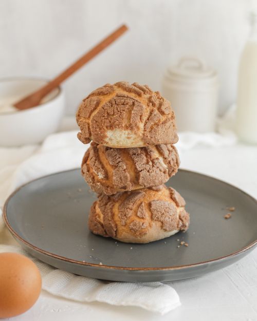 Free Three Mexican conchas stacked on a plate with rustic kitchenware in the background. Stock Photo