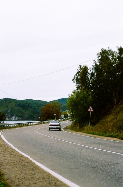 Free A car travels on a winding road surrounded by lush greenery under an overcast sky. Stock Photo