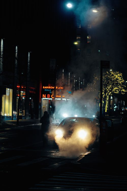 Free A car emits smoke on a dimly lit urban street at night, conveying a moody atmosphere. Stock Photo