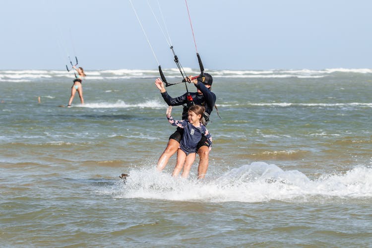 A Child Waving While Kitesurfing With An Adult