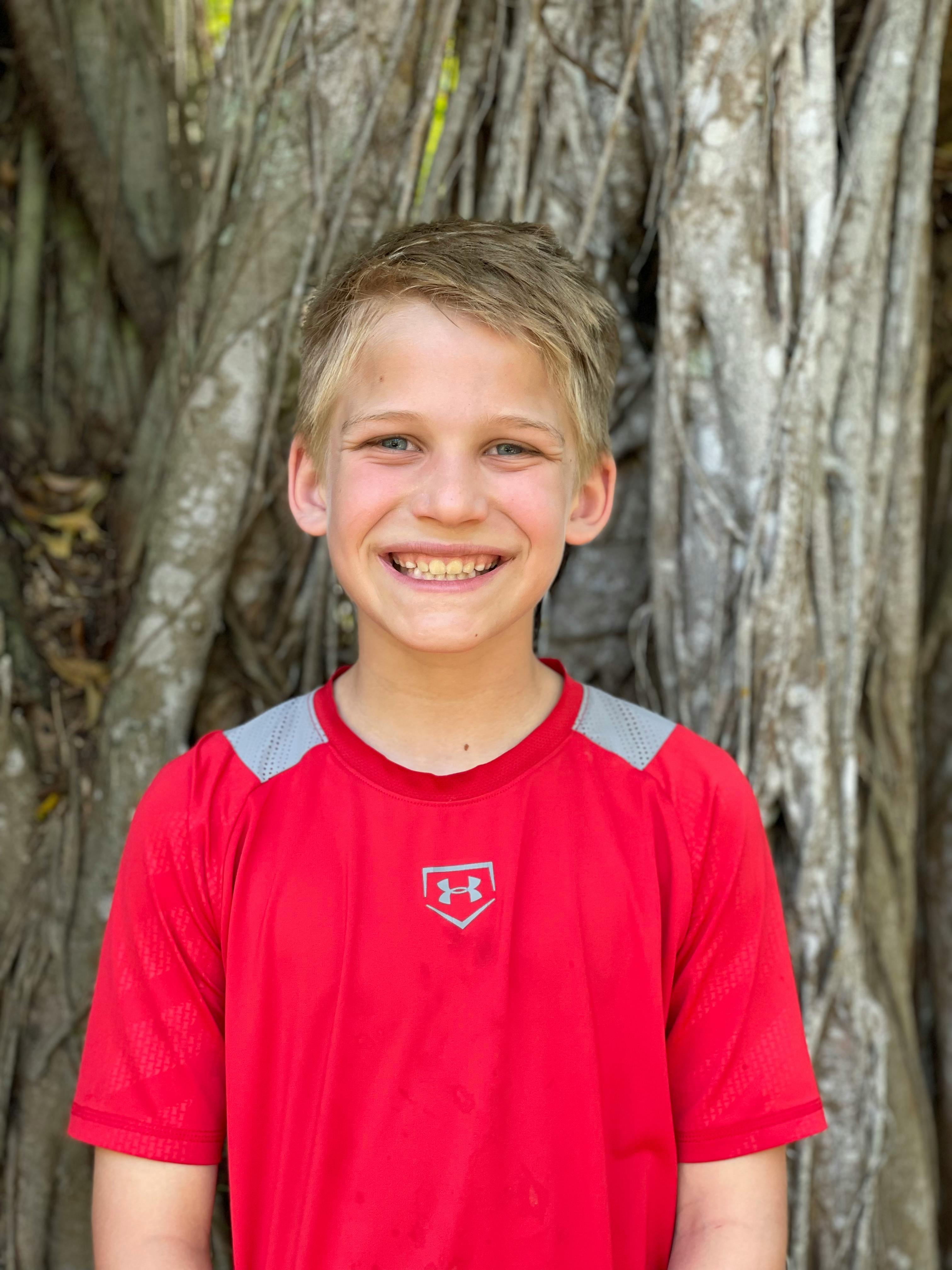 Happy boy smiling in front of tree roots outdoors on a sunny day.