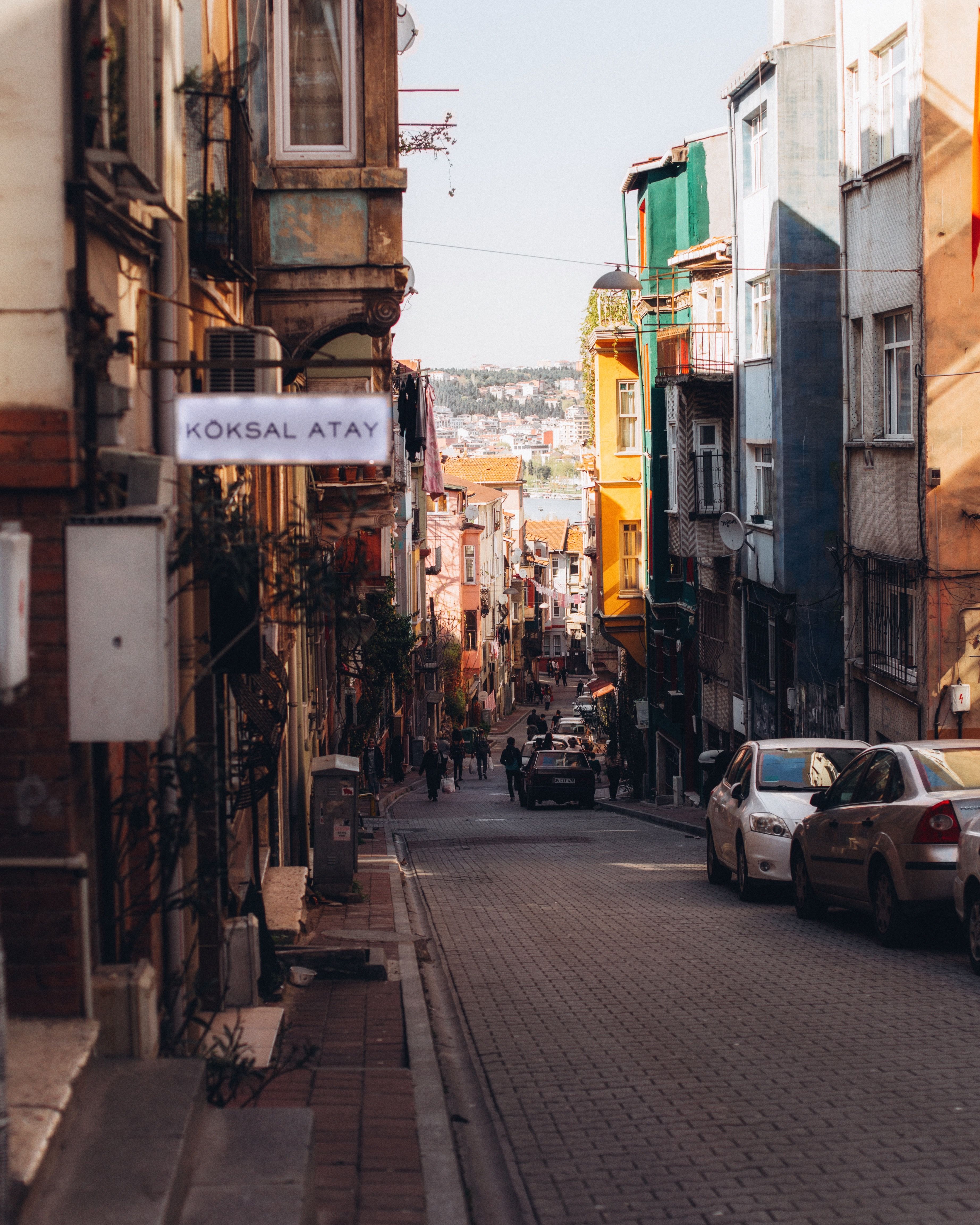 A vibrant street view showcasing colorful buildings and parked cars in an urban neighborhood. People strolling create a lively atmosphere.