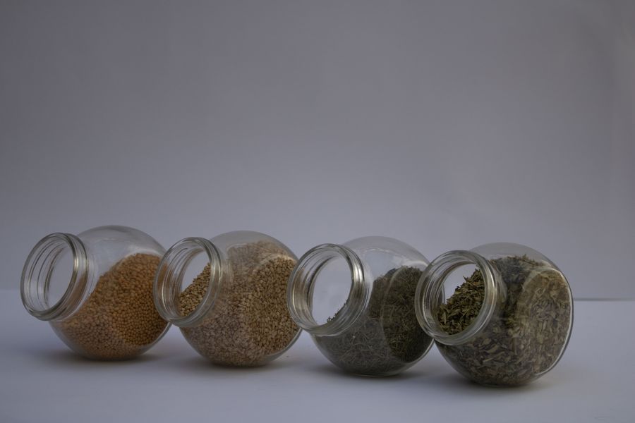 Four glass jars containing different spices and herbs, arranged on a plain background.