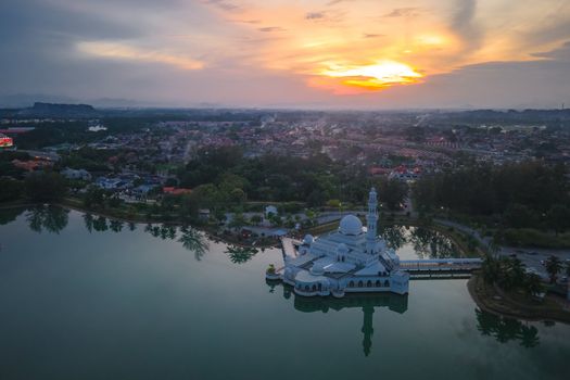 Stunning aerial view of Tengku Tengah Zaharah Mosque reflecting in a serene lake at sunset.