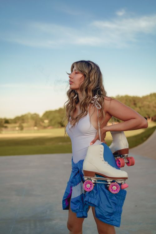 Free Young woman holding roller skates outdoors on a sunny day. A casual and sporty lifestyle scene. Stock Photo