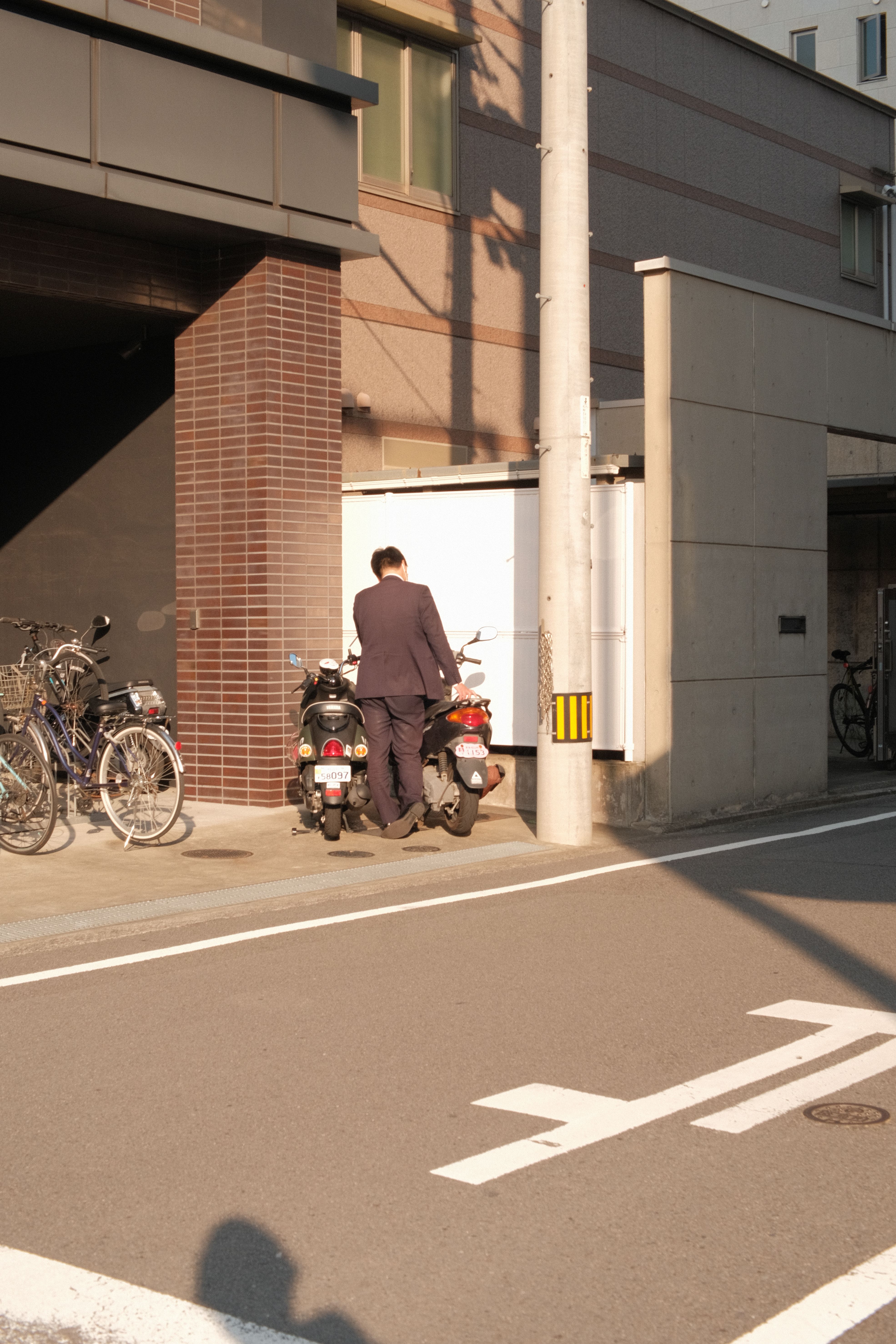 A businessman in a suit parks a motorcycle in a sunlit urban street.
