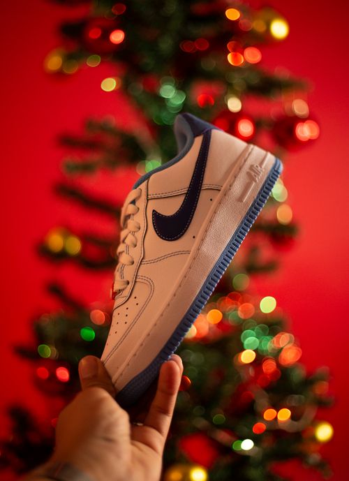 Free Close-up of a Nike Air Force 1 shoe held in front of a festive Christmas tree background. Stock Photo