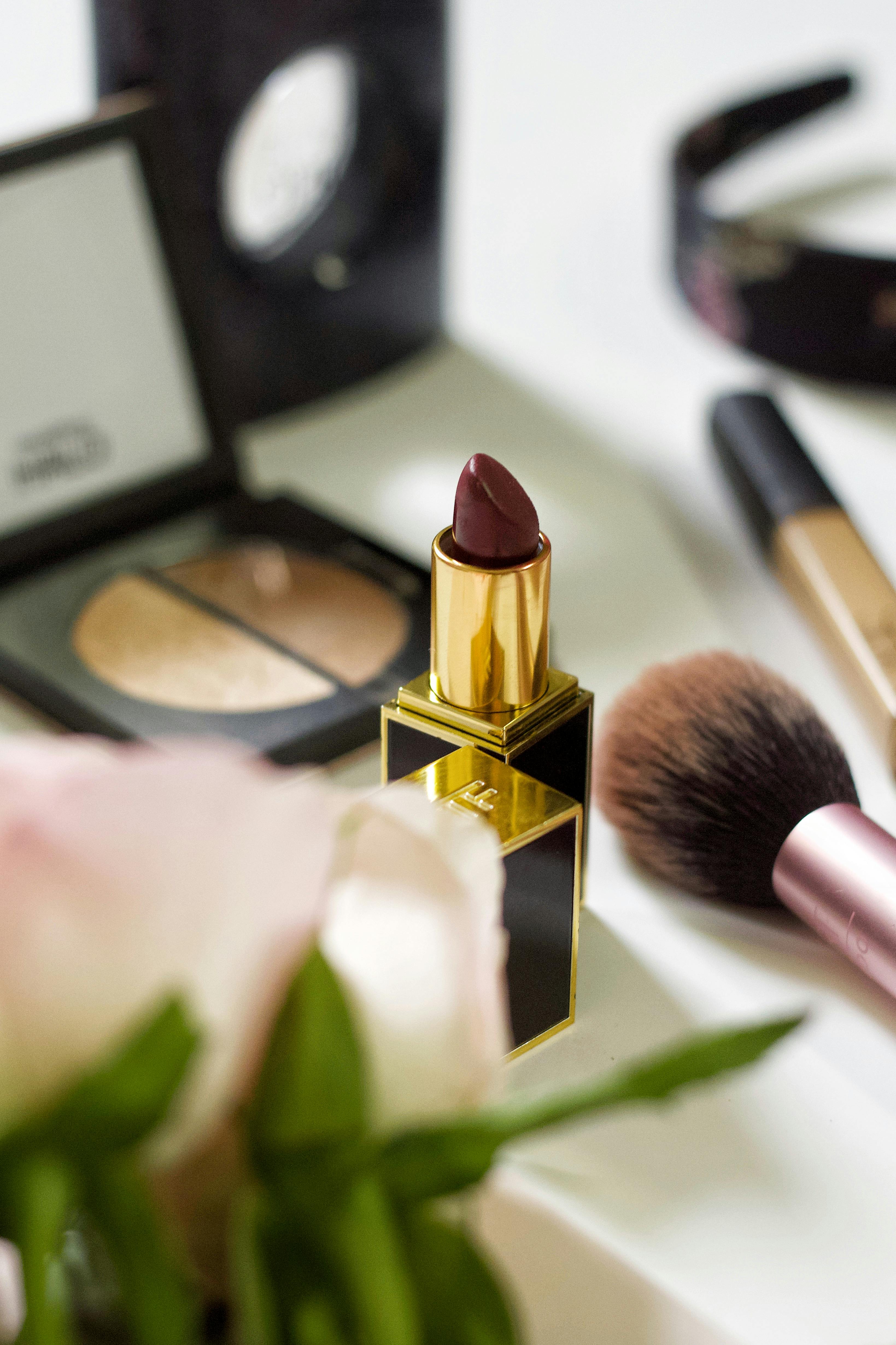 Stylish arrangement of cosmetics including lipstick, eyeshadow, and brushes.