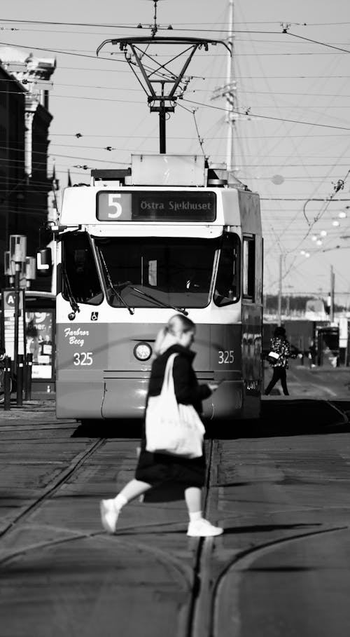 Grayscale Photo of Person Walking on Street Near Tram