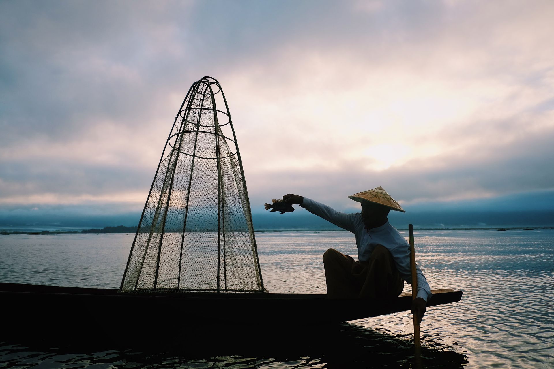 Silhouette of a fisherman in Shan, Myanmar, casting a net at sunset on Inle Lake.
