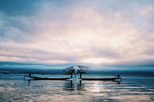 Fishermen casting nets in silhouette during dawn on a calm sea, exuding serenity and traditional lifestyle.