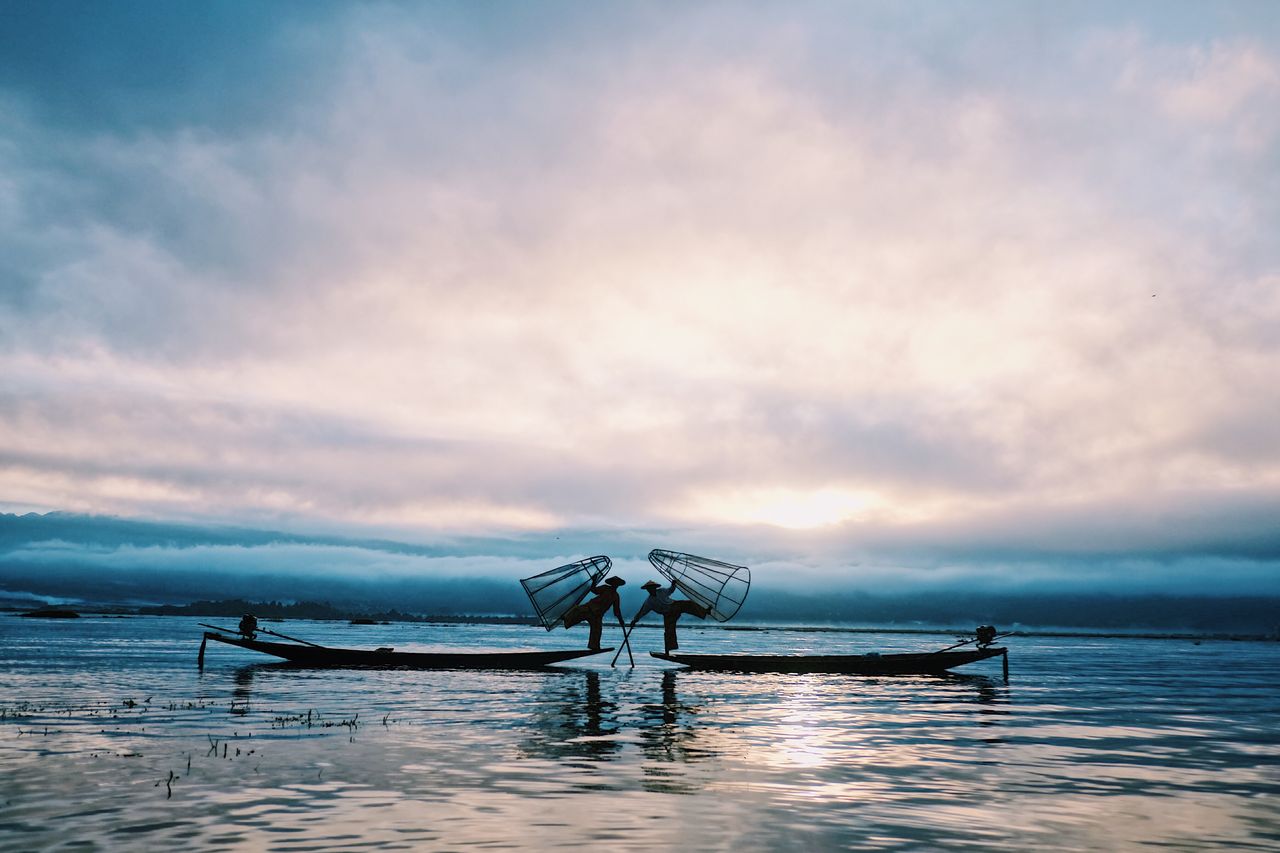 fishermen casting nets in silhouette during dawn on a calm sea exuding