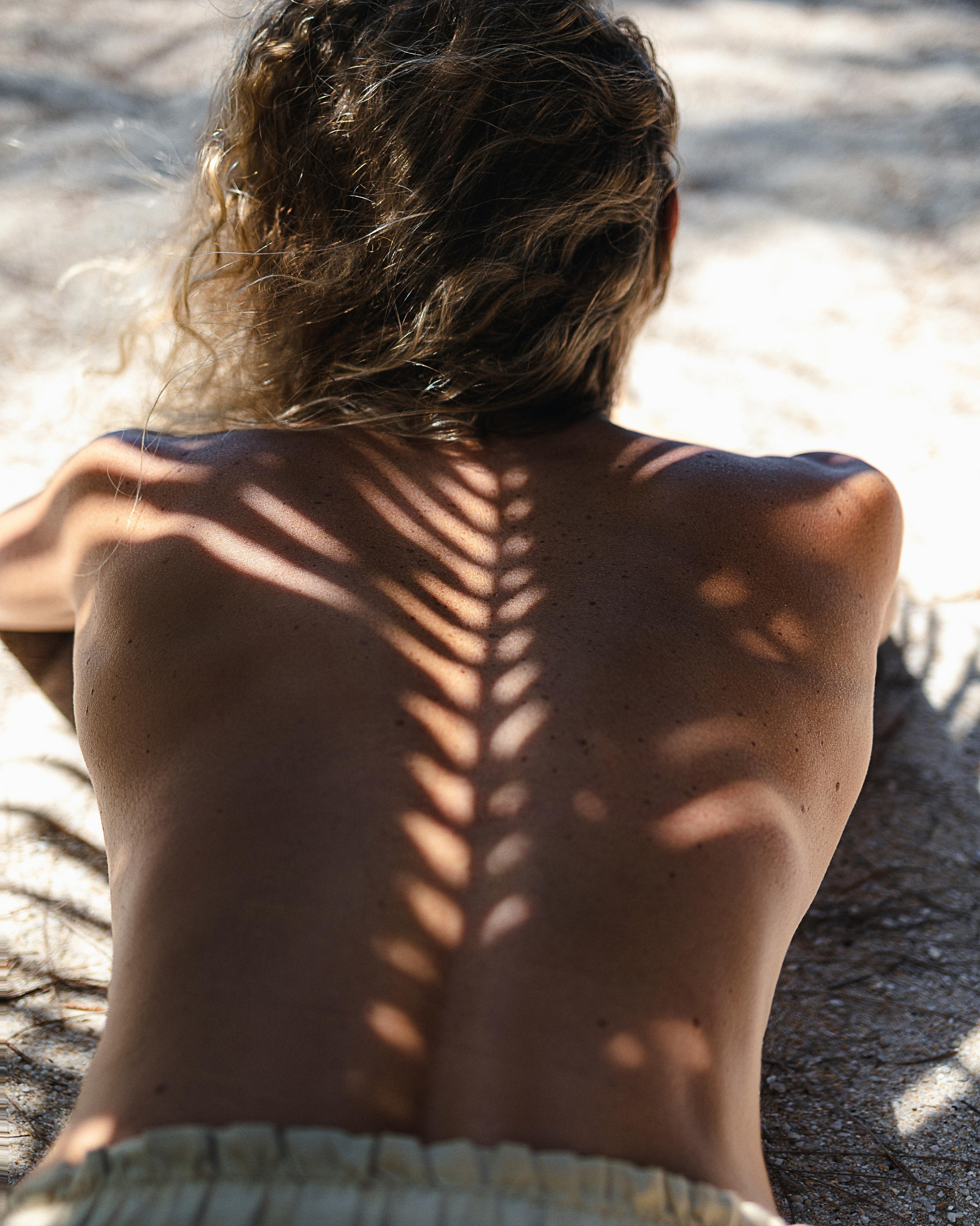 Back view of a woman sunbathing on a sandy beach in Thailand, enjoying the summer sun.