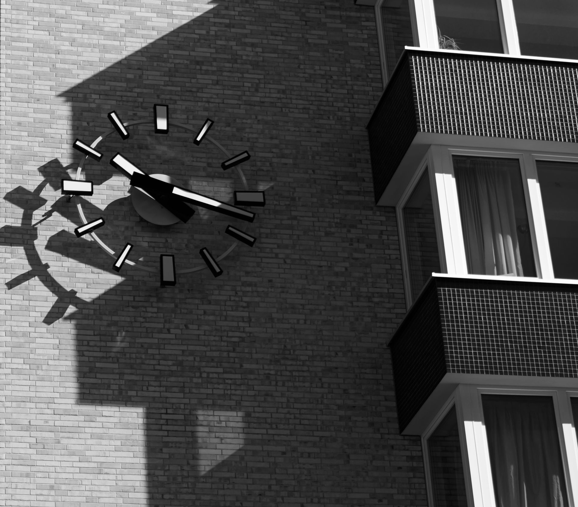 Monochrome image of a clock casting shadows on a modern brick building.
