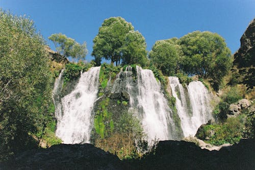 Low Angle Shot of Waterfalls Near Green Trees Under Blue Sky