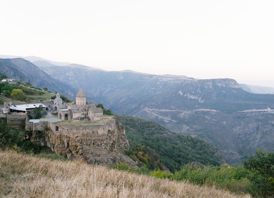 Scenic view of a medieval monastery perched on a cliff over a stunning mountainous valley landscape.