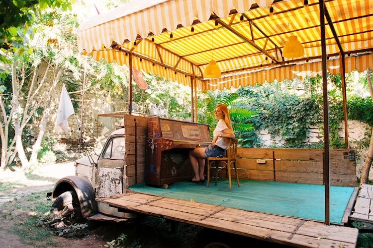 Blonde Woman Sitting By Piano On Truck In Garden