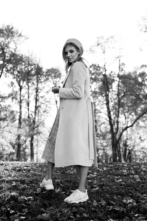 Free Black and white portrait of a fashionable woman in a coat and sneakers, exploring a park during fall. Stock Photo