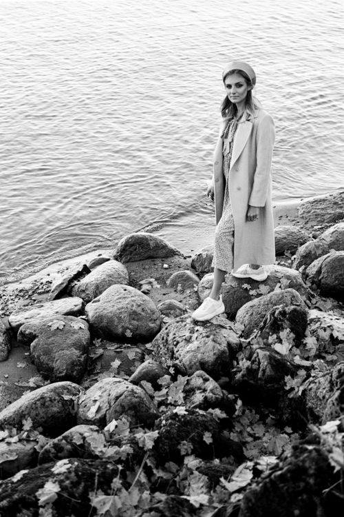 Free A stylishly dressed woman stands among rocks by the sea, exuding elegance in a black and white image. Stock Photo