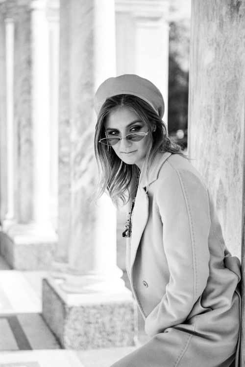 Free Black and white portrait of a fashionable woman sitting outdoors, wearing sunglasses and a beret. Stock Photo